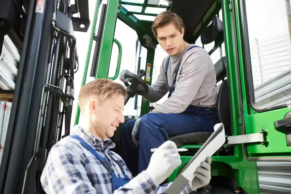 two men in overalls seated on a forklift
