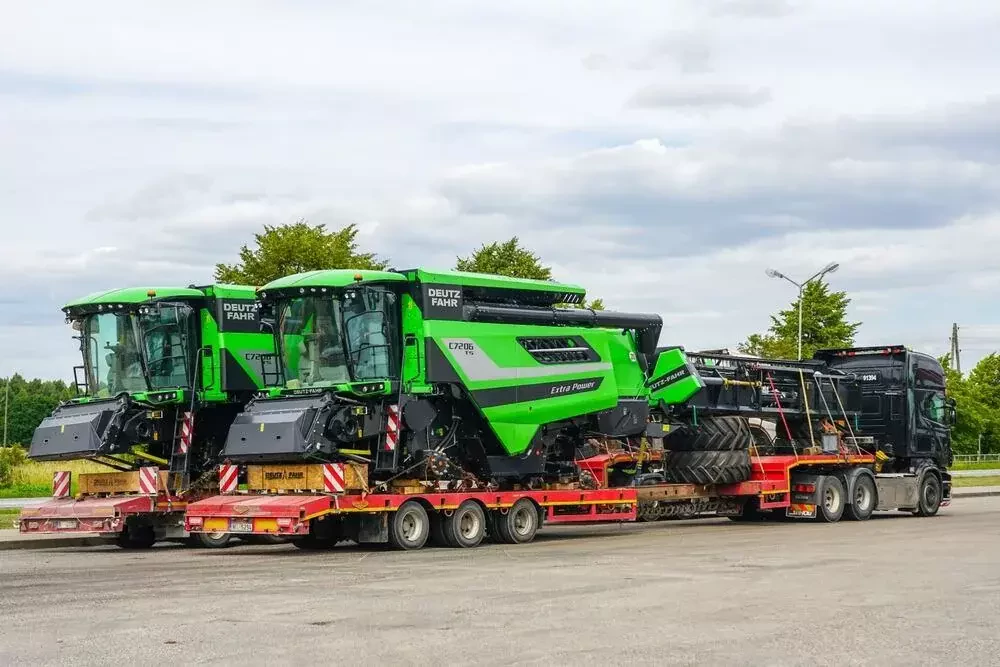 a green tractor hauler loaded with two large green tractors