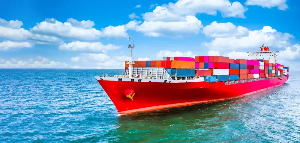 red cargo vessel with colorful containers on blue sea