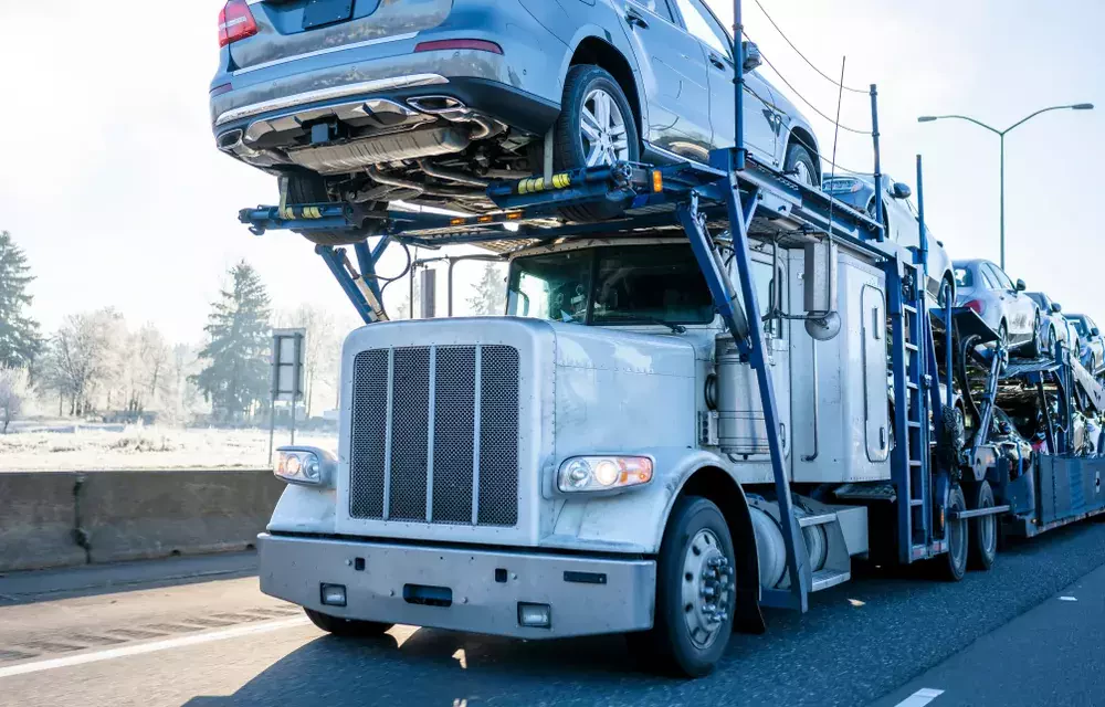 truck carrying several vehicles on a road under the sky